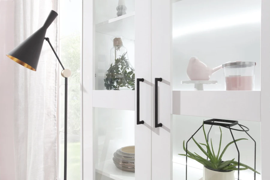 Moderne weiße Glasvitrine mit markanten schwarzen Griffen und dekorativem Inhalt im Wohnzimmer.