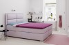Lavendelfarbenes Boxspringbett in hellem Schlafzimmer mit lila Tagesdecke und Deko.