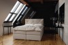 Modernes weißes Boxspringbett in hellem Dachzimmer mit großen Fenstern und Holzboden.