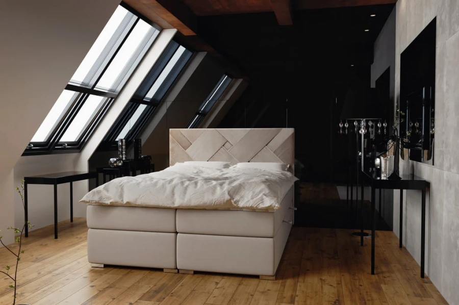 Modernes weißes Boxspringbett in hellem Dachzimmer mit großen Fenstern und Holzboden.