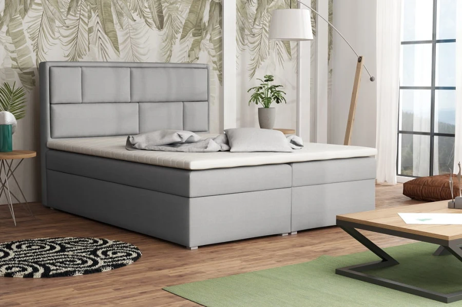 Modernes Boxspringbett in Hellgrau mit gepolstertem Kopfteil in einem hellen Schlafzimmer.