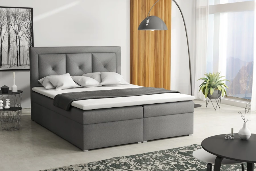 Graues Boxspringbett mit gepolstertem Kopfteil in modernem Schlafzimmer.
