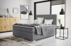Modernes Boxspringbett in Grau mit hohem Kopfteil in einem hell eingerichteten Schlafzimmer.