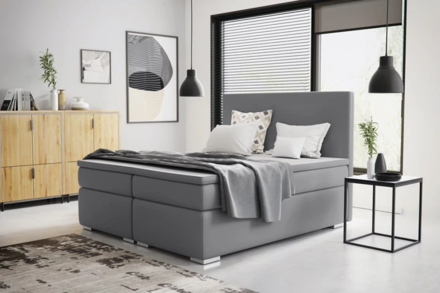 Modernes Boxspringbett in Grau mit hohem Kopfteil in einem hell eingerichteten Schlafzimmer.