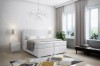 Weißes Boxspringbett mit gestepptem Kopfteil in einem lichtdurchfluteten, modernen Schlafzimmer.