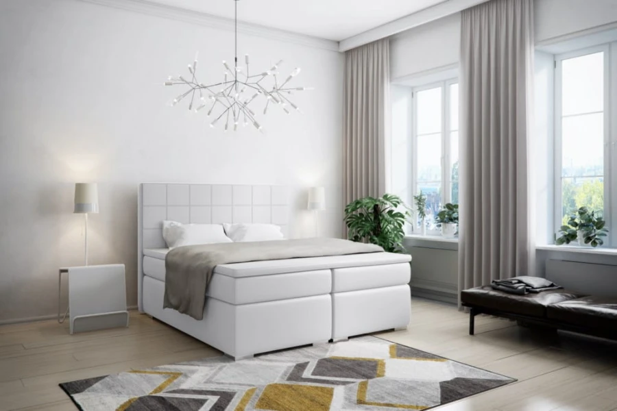 Weißes Boxspringbett mit gestepptem Kopfteil in einem lichtdurchfluteten, modernen Schlafzimmer.