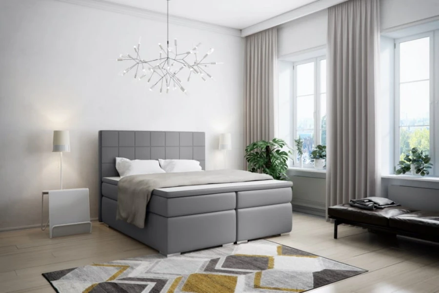 Graues Boxspringbett mit Karosteppung im Kopfteil in hellem Wohnambiente mit Design-Leuchte.