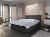 Dunkelgraues Boxspringbett mit Polsterkopfteil und moderner Bettwäsche in einem hellen Schlafzimmer.