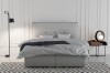 Modernes hellgraues Boxspringbett mit dekorativem Kopfteil im Schlafzimmer.