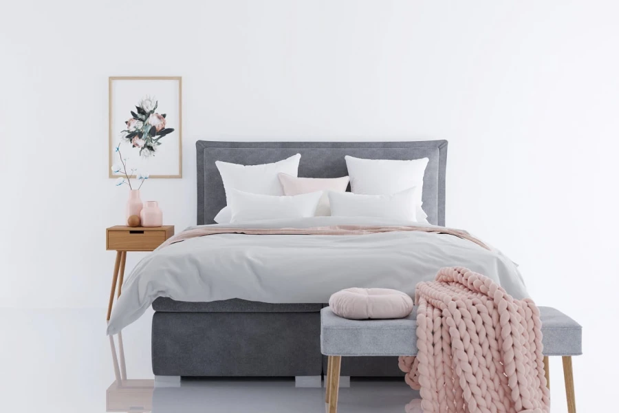 Hell eingerichtetes Schlafzimmer mit grauem Boxspringbett, rosa Decke und minimalistischer Deko.