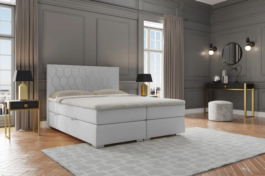 Hellgraues Boxspringbett mit gestepptem Kopfteil in stilvollem Schlafzimmer-Ambiente.