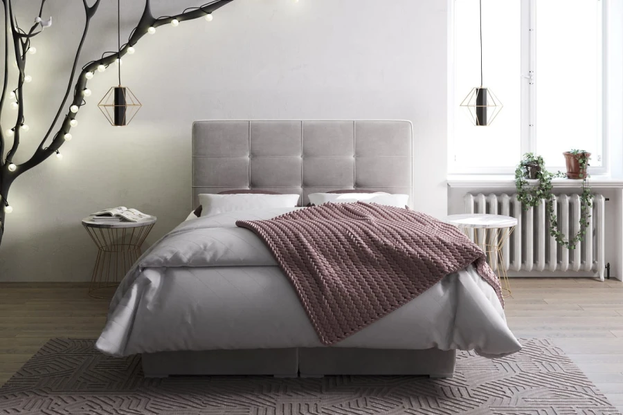 Gemütliches graues Polsterbett mit rosa Strickdecke und modernem Stepp-Kopfteil.