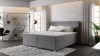 Elegantes graues Boxspringbett mit weißem Topper im modernen Wohnambiente.