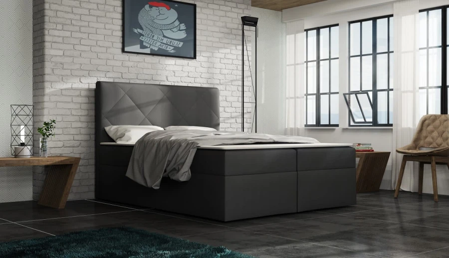 Elegantes Polsterbett in Grau vor weißer Ziegelwand in einem hellen Zimmer.