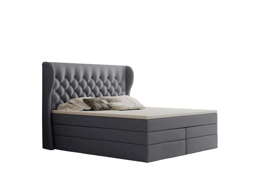 Graues Boxspringbett mit gestepptem Kopfteil vor weißem Hintergrund