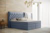 Hellblaues Boxspringbett mit elegantem Kopfteil und Knopfheftung vor einer hellen Holzwand.