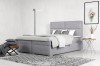 Graues Doppelbett in Boxspring-Optik mit weichem Polsterbezug und passender Dekoration.