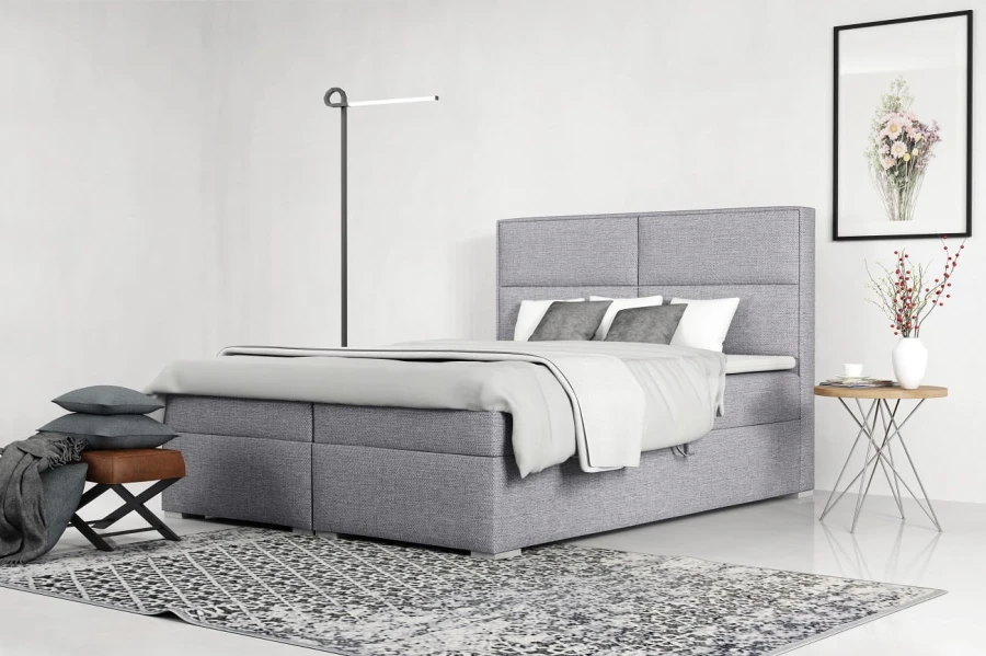 Graues Doppelbett in Boxspring-Optik mit weichem Polsterbezug und passender Dekoration.