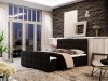 Dunkelgraues Boxspringbett mit Knopfsteppung vor einer markanten dunklen Steinwand.