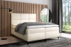 Cremefarbenes Boxspringbett in modernem Design mit gemütlicher grauer Decke.
