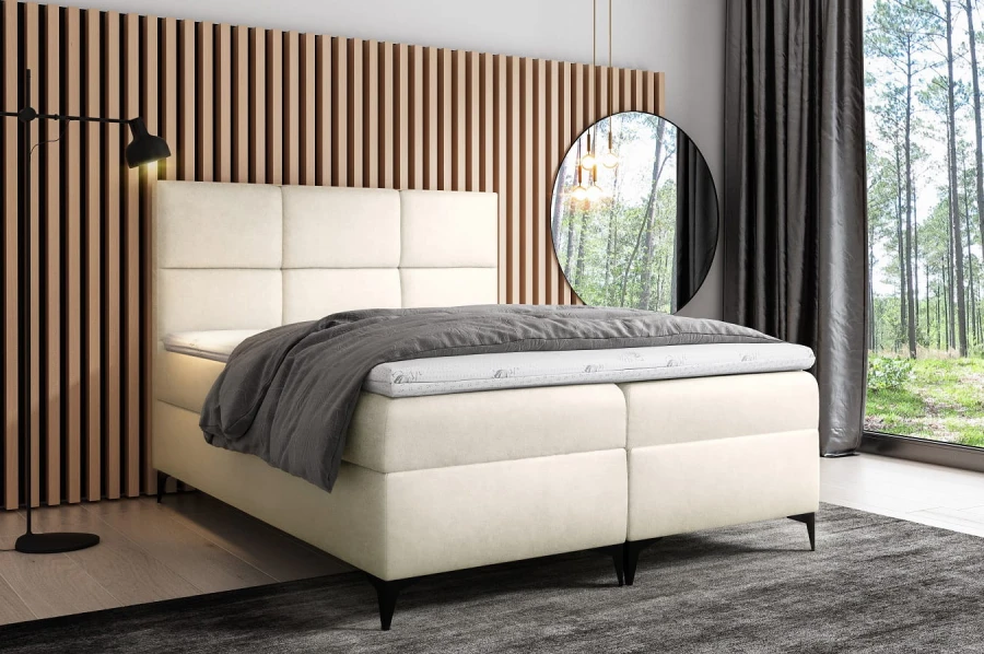 Cremefarbenes Boxspringbett in modernem Design mit gemütlicher grauer Decke.
