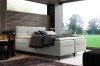 Modernes weißes Boxspringbett in einem hellen Schlafzimmer mit Gartenblick.
