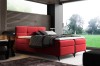 Rotes Boxspringbett in modernem Design vor einer Lamellenwand aus Holz.