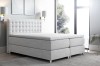 Hellgraues Boxspringbett mit stilvoller Steppung und weißer Matratzenauflage.