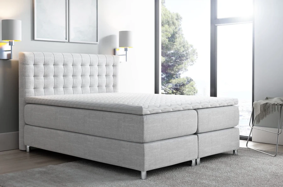Hellgraues Boxspringbett mit stilvoller Steppung und weißer Matratzenauflage.