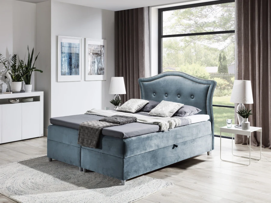 Hellblaues Boxspringbett aus Samt mit dekorativem Kopfteil und Bettkasten.