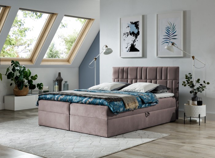 Altrosa Boxspringbett mit gestepptem Kopfteil in einem hellen Schlafzimmer unter Dachschrägen.