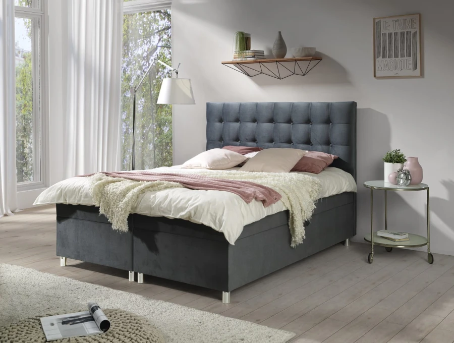 Boxspringbett in Dunkelgrau mit dekorativer Steppung am hohen Kopfteil.