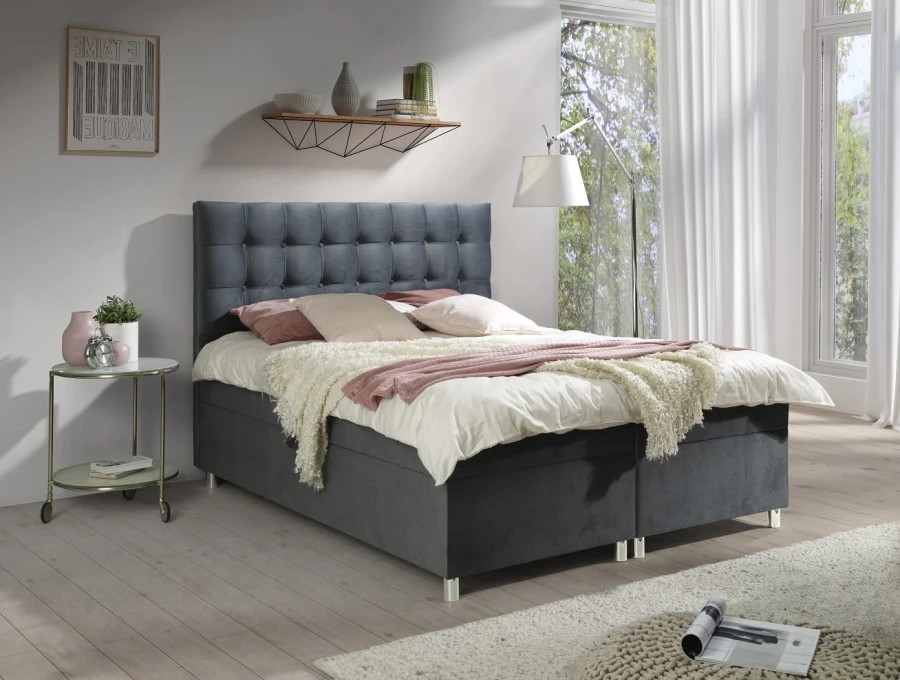 Graues Boxspringbett mit gestepptem Kopfteil und gemütlicher Bettwäsche im Schlafzimmer