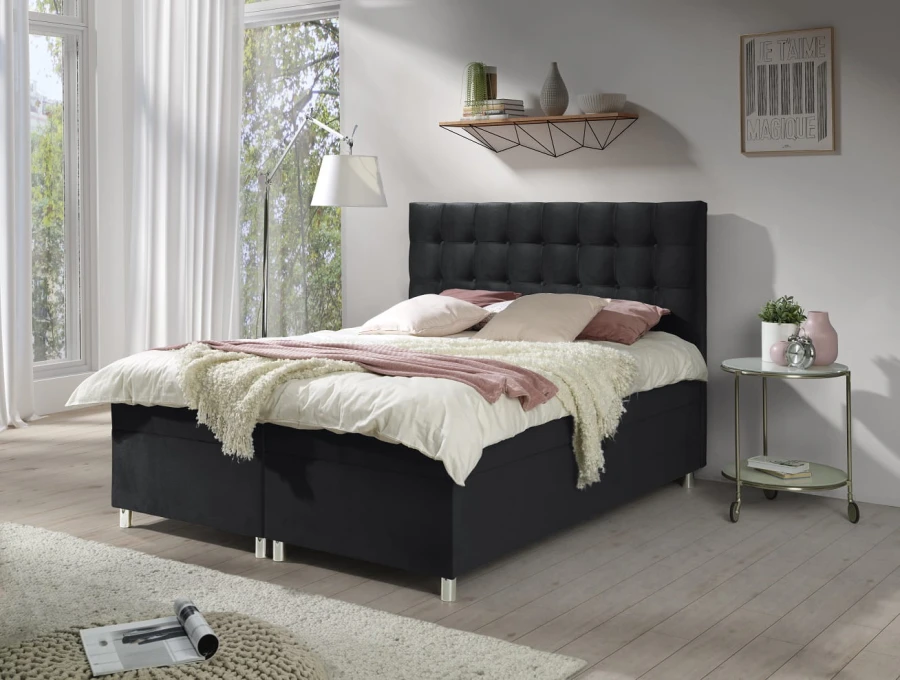 Schwarzes Boxspringbett mit gepolstertem Kopfteil und weißer Bettwäsche im hellen Schlafzimmer.
