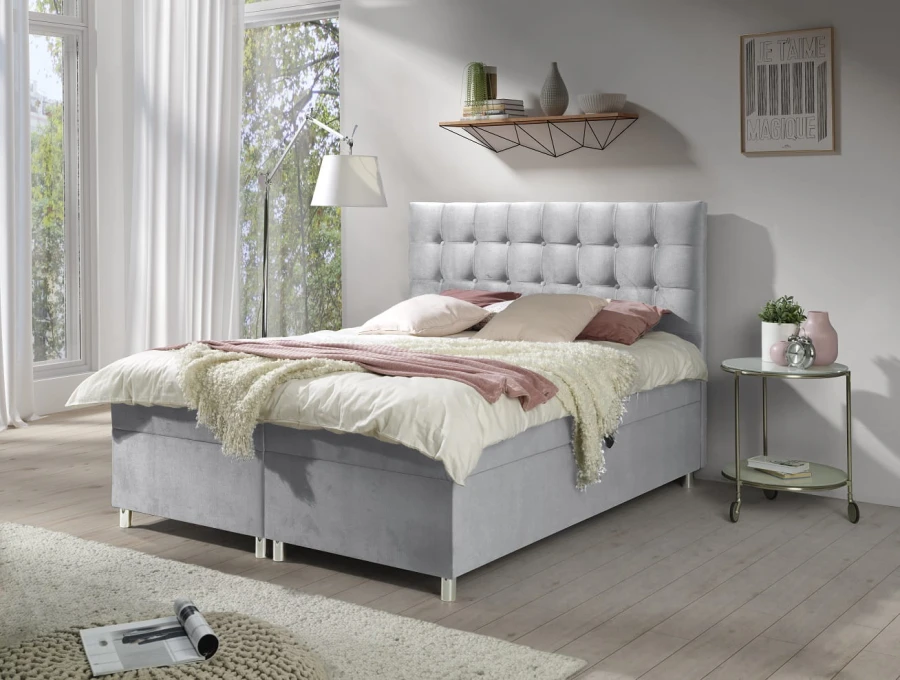 Hellgraues Boxspringbett mit Knopfsteppung am Kopfteil für ein modernes Schlafzimmer.