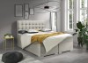 Beiges Boxspringbett mit gelber Decke, dekorativer Pflanze und moderner Deckenleuchte.