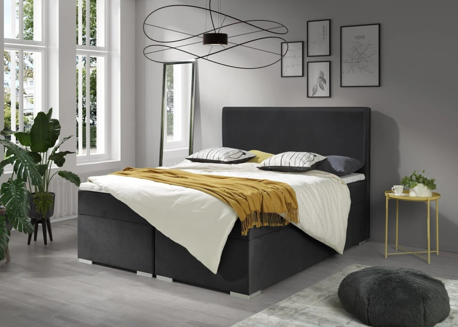 Modernes dunkelgraues Boxspringbett mit gelber Tagesdecke in einem hellen Schlafzimmer.