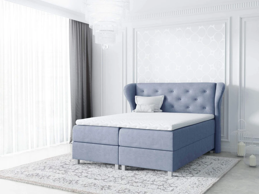 Blaues Boxspringbett mit gestepptem Kopfteil in einem hellen, modernen Schlafzimmer.