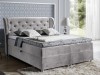 Hellgraues Boxspringbett mit Ohrensessel-Kopfteil und Samtbezug in einem hellen Schlafzimmer-Ambiente.