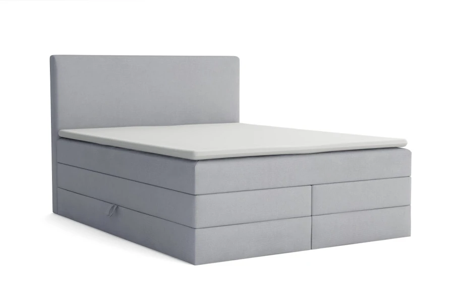 Hellgraues Boxspringbett mit schlichtem Kopfteil und Topper vor weißem Hintergrund freigestellt.