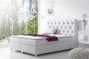 Modernes weißes Boxspringbett mit gestepptem Kopfteil und roter Decke in hellem Schlafzimmer.