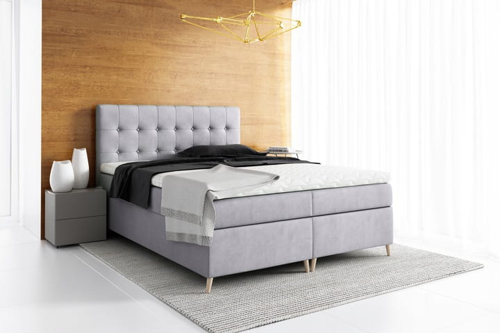 Hellgraues Boxspringbett mit hohem Kopfteil vor Holzwand.