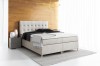 Modernes Boxspringbett in Beige mit gestepptem Kopfteil in einem hellen Schlafzimmer.