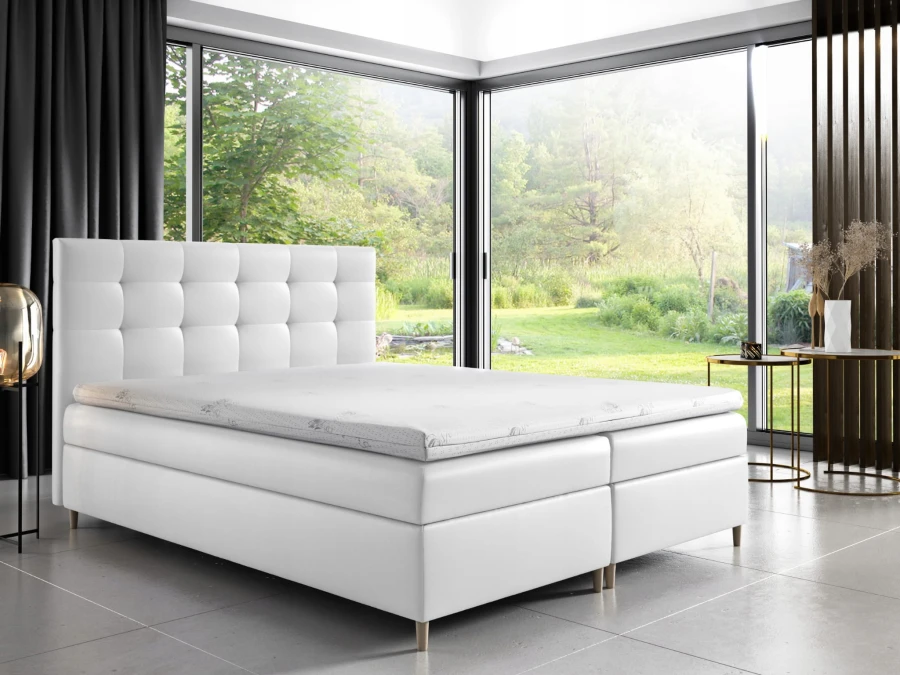 Weißes Boxspringbett mit gestepptem Kopfteil in modernem Schlafzimmer mit Gartenblick.