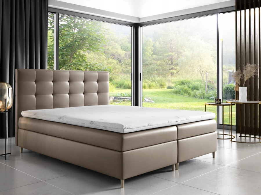 Beiges Boxspringbett mit Karosteppung am Kopfteil vor einem großen Panoramafenster.