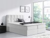 Minimalistisches weißes Boxspringbett mit hohem Kopfteil in hellem Raumambiente.