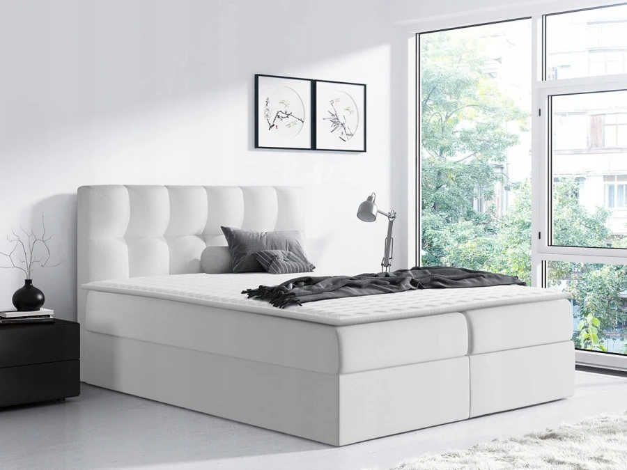 Minimalistisches weißes Boxspringbett mit hohem Kopfteil in hellem Raumambiente.