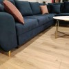 Nahaufnahme eines blauen Samtsofas mit rosa Kissen und goldenen Standfüßen auf Parkett.