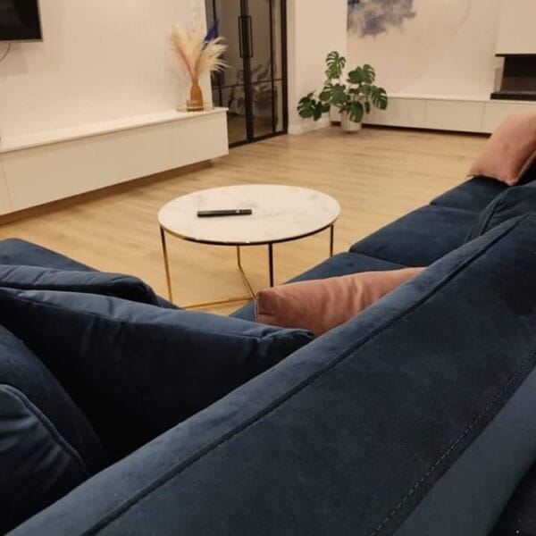 Modernes Wohnzimmer mit blauem Samtsofa, rosa Kissen und rundem Marmortisch.