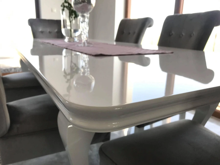 Nahaufnahme eines weißen Hochglanz-Esstisches mit elegant abgerundeter Kante.